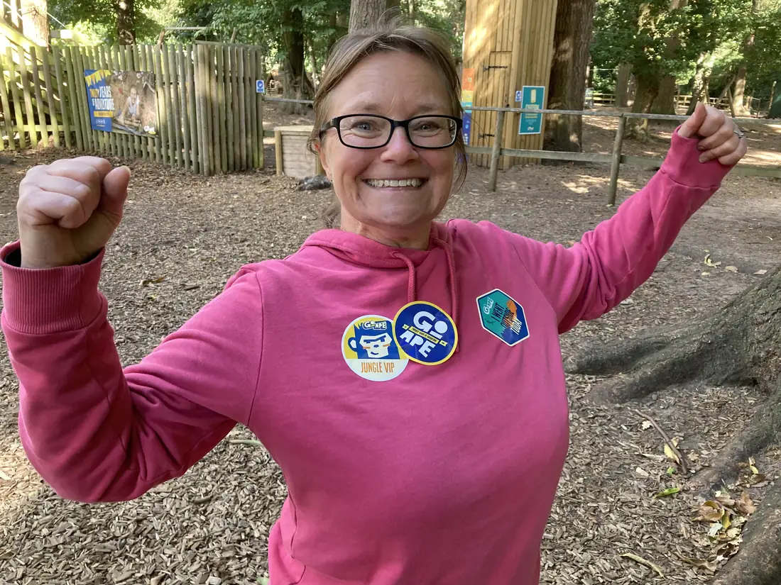 Philly at Go Ape in a pink hoodie, fists raised and smiling